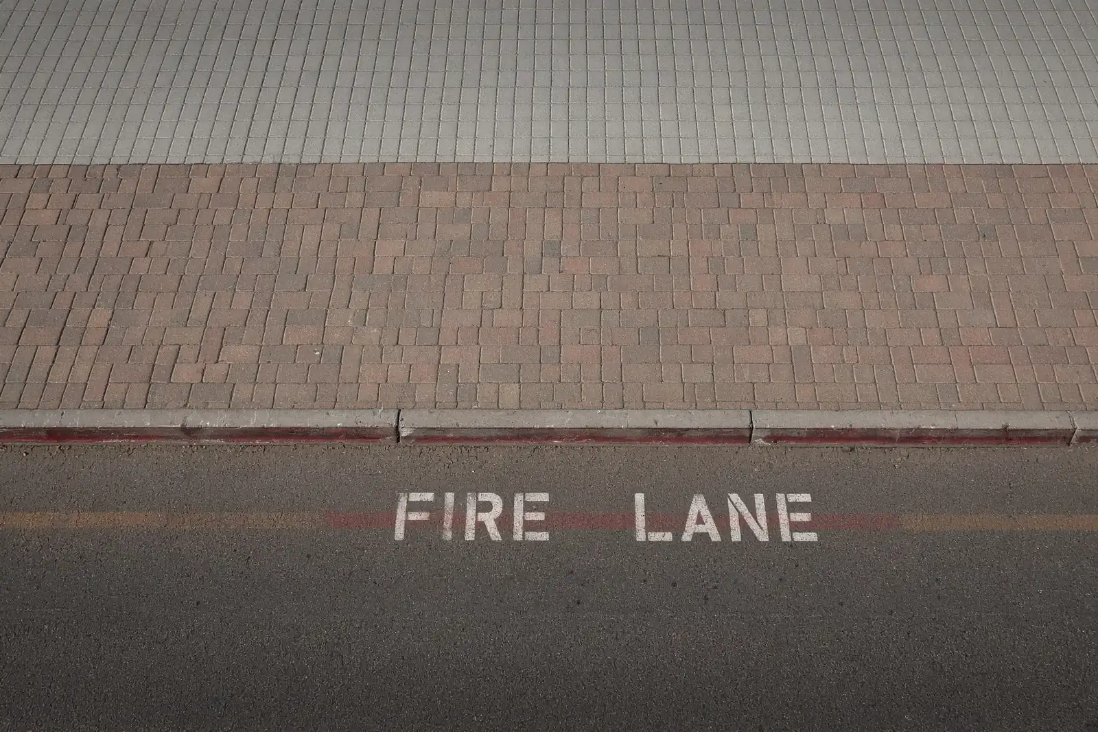Red fire lane curb with FIRE LANE stencilled in white on the asphalt beside a commercial building