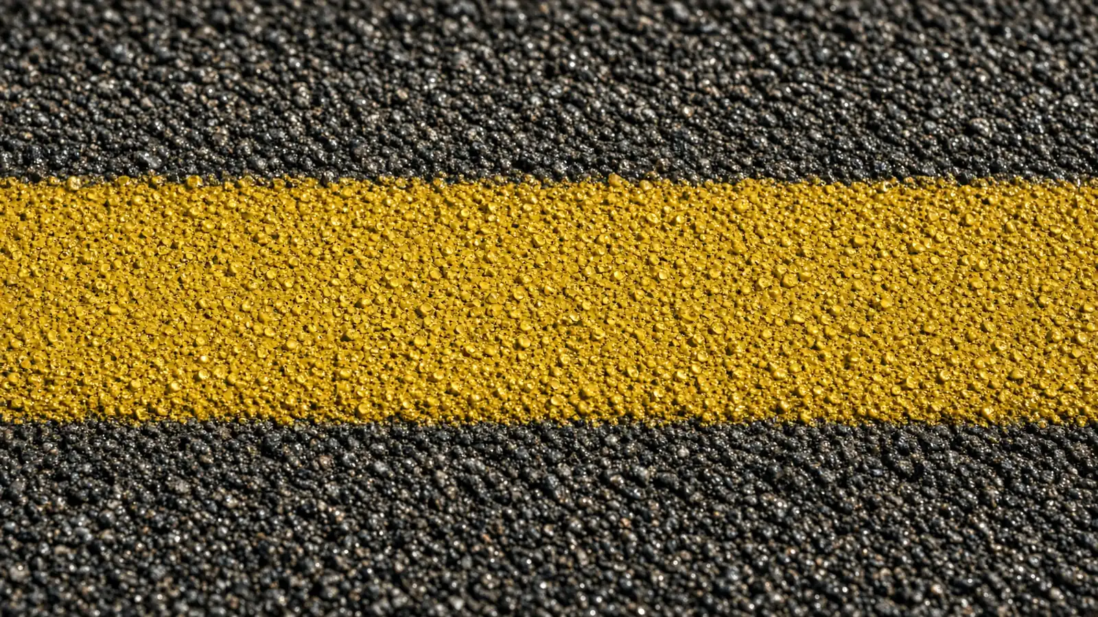 Close-up of a freshly painted yellow parking lot line over coarse asphalt